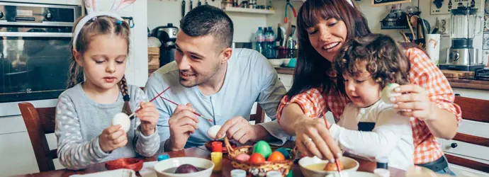 Család ül a konyhaasztalnál húsvéti tojást festve