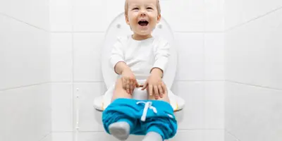 Ein kleines Kind sitzt mit heruntergelassener blauer Hose auf einer Toilette