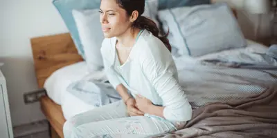 Eine Frau sitzt mit Schmerzen im Unterleib auf einem Bett