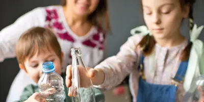 O familie tânără și zâmbitoare sortează sticlele de plastic și de sticlă pentru a le recicla.