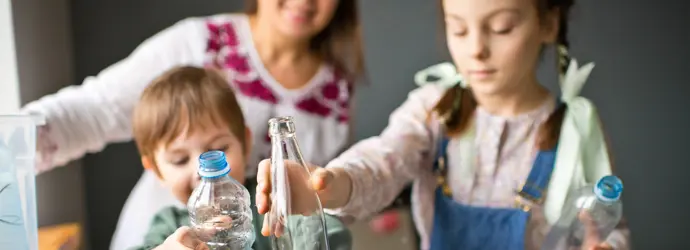 O familie tânără și zâmbitoare sortează sticlele de plastic și de sticlă pentru a le recicla.