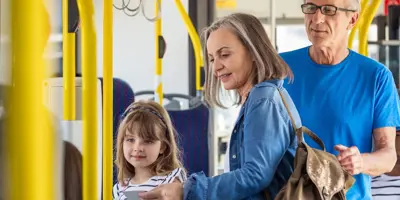 Familie cu copil urcând în autobuz, pe șine galbene.